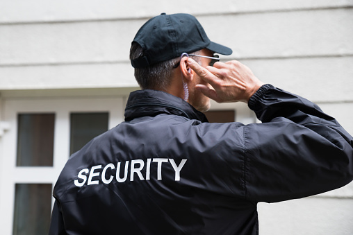 Rear view of mature security guard listening to earpiece against building